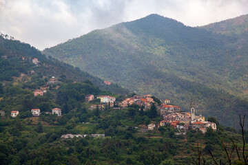 Fototapeta premium Beautiful views of the Italian village in the mountains. Temples and rooftops among the greenery. Low clouds after rain.