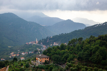 Fototapeta na wymiar Beautiful views of the Italian village in the mountains. Temples and rooftops among the greenery. Low clouds after rain.