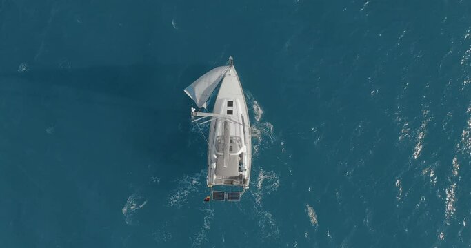 Yacht with reflection sailing on open sea aerial. Nobody nature seascape with sail boat cruising at ocean bay. Mountain landscape of Arran Island, Scotland. Cinematic summer vacation scenery.