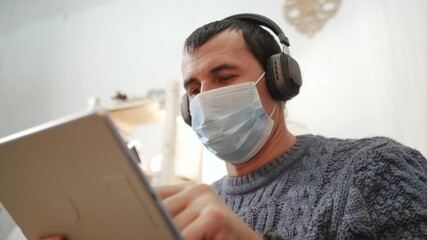 telework. man in a medical mask works remotely in a digital tablet wearing a medical protective freelance mask. office home telework concept. man in a medical protective mask works at home