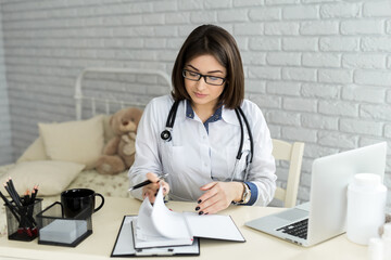 Doctor working with laptop computer and writing on paperwork. Hospital background.