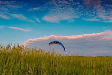 Parachute canopy over spring green grass hill under beautiful blue sky with clouds.