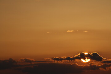 the photo was taken during sunset, from the bottom left is the disc of the sun behind the cloud, the sky is orange