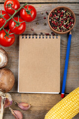 Notepad and pencil with vegetables on a wooden background. Space for text.