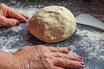 manos de mujer mayor trabajando una masa sobre una mesada negra de piedra para hacer pan casero