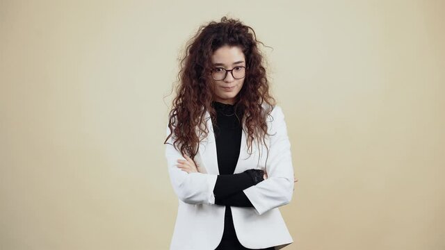 Upset young woman with curly hair, holds her hands in the middle and looks contemptuously into the room. Young hipster in gray jacket and white shirt, with glasses posing isolated on beige background