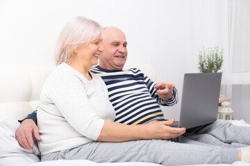 handsome senior couple woman and man sitting in bed using laptop at home.