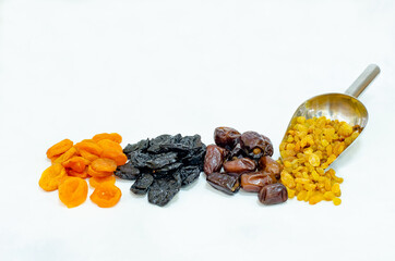 Dried fruits - dates, dried apricots, prunes, raisins on a white background, with an iron spatula