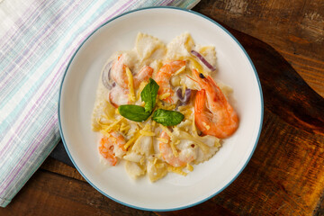 Pasta with shrimps in a creamy sauce on a gray plate on a wooden table on a napkin.