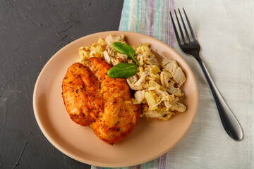 Baked chicken breast with salad on a plate decorated with spinach next to a fork on a concrete background on a gray napkin.