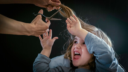 Little boy, toddler is afraid and doesn't want to cut his hair. A baby boy is fearful of getting...