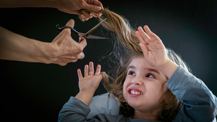 Little boy, toddler is afraid and doesn't want to cut his hair. A baby boy is fearful of getting...