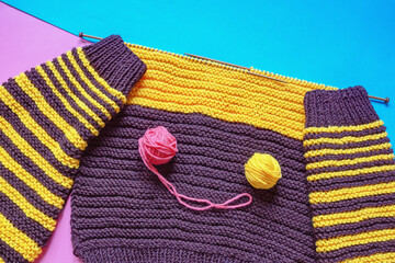 Home hobbies concept. Unfinished yellow and brown knitting, balls of wool and knitting  needles on blue and pink background. Copy space