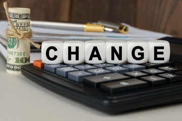 There are cubes on the calculator that say - CHANGE. Nearby out of focus - dollars, notebook and pen