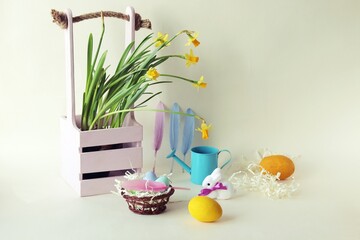 Easter eggs, blooming daffodils, toy hares on a light background, decorating a home interior for the holiday