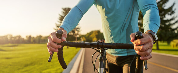 Website header of Getting ready to ride. Cropped shot of a road bicycle racer in sportswear standing on the road in park at sunset, cycling outdoors