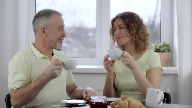 An elderly couple is having breakfast and talking at a table by the window.