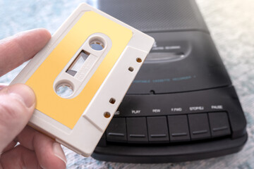 Obraz premium hand with a music cassette with blank label in foreground and black portable compact cassette recorder from the 80s in background - image