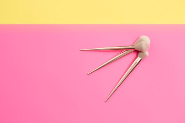 top view of make-up brushes of different sizes on a pink and yellow background