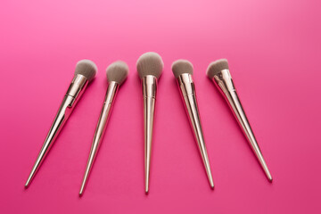 make-up golden brushes of different sizes on a pink background