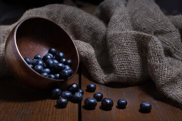 Ripe blueberry pouring out from wooden bowl on brown background with burlap cloth. Rustic still life.
