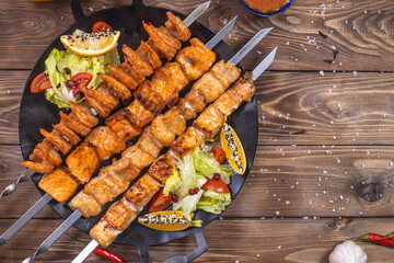 Minced kebab on a metal skewer with sauce, sliced cucumbers, tomatoes and onions.