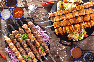 Minced kebab on a metal skewer with sauce, sliced cucumbers, tomatoes and onions.