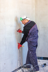 An electrician is laying a cable in an electrical wiring ditch