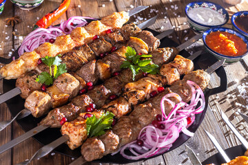 Minced kebab on a metal skewer with sauce, sliced cucumbers, tomatoes and onions.