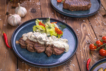 Beef patty on a platter with vegetables, lettuce, bell pepper, rosemary, garlic and sesame seeds on a brown wooden background.