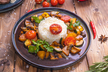 Rice on a plate with stewed vegetables on a wooden background decorated with rosemary, chili pepper, spices.