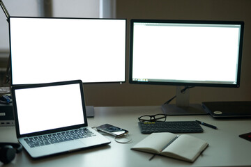 Fototapeta premium Many blank white screen of computer monitors with accessories and work tools on modern freelance working space