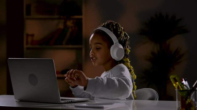 A Girl In White Headphones Listens To Music, Singing Along With It, Plays Online Games On Her Laptop. The Child Sits At A Table In Front Of A Laptop In The Room. Close Up. Slow Motion Ready 59.97fps.