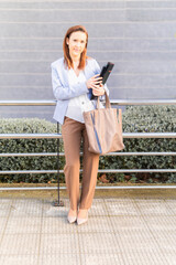 Obraz premium Young adult woman smiling beautiful businesswoman waited on the street for a client with laptop and folder. successful business woman concept. copy space