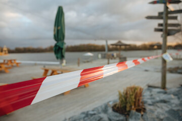 Locked beach on a lake in Germany. Sandy beach with chairs and a barrier tape. red and white striped warning tape in front of a lake. recreational area closed during a pandemic 