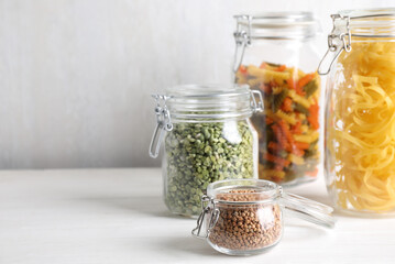 Jars with buckwheat, peas and pasta on white table. Space for text