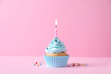 Delicious birthday cupcake with burning candle and sprinkles on pink background