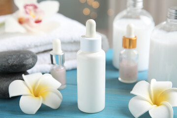Beautiful spa composition with essential oil and plumeria flowers on turquoise table against blurred lights, closeup
