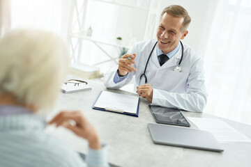 Obraz premium Cheerful male doctor talking with elderly woman in his office