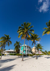 Fototapeta na wymiar Tropical white sand beach with coco palms and the turquoise sea on Caribbean island. Pastel color houses pink, green, blue. Little Cayman, Cayman Islands