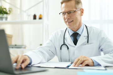 Cheerful doctor using modern notebook in clinic