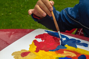 the child draws with a brush with acrylic paints of different colors