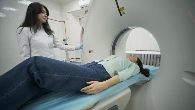 Female patient is undergoing CT or MRI scan under supervision of a radiologist in modern medical clinic. Patient lying on a CT or MRI scan bed, moving outside the machine.