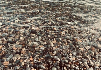 Fascinating background from colorful pebbles on the beach. some parts are still covered with water while while the tide is lower.