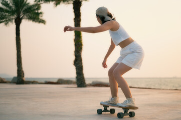 Asian Beautiful women surf skate or skateboard outdoors on beautiful summer day. Happy young women play surf skate at park near the beach on morning time. Sport activity lifestyle concept.