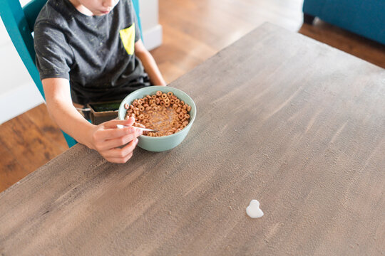 Boy Eating Breakfast In Kitchen While On A Tablet