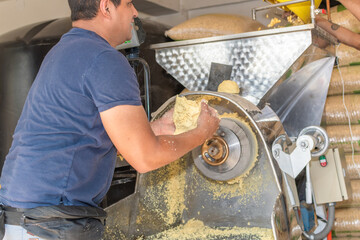 front view of a nixtamal mill while a man takes out the dough that is being produced