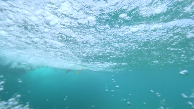 UNDERWATER, SLOW MOTION: Intimidating seaside scenery of wave violently carrying surfboard. Powerful ocean swell forcefully crashing while pro surfboarder carves it with ease. Cool underwater scenery.