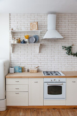 White classic kitchen with brick wall. Shelf with grocery products. Cereals, pasta and plates on a white wooden shelf. Modern kitchen stylish interior with cozy open shelf, white gas stove, oven