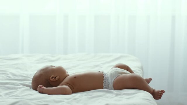 Cute newborn african american baby in diaper sleeping on big bed at home, side view